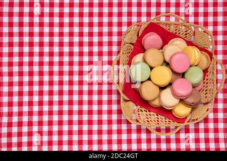Gebäck, Desserts und Süßigkeiten. Draufsicht auf die original französischen Makronen-Kekse in einem Korb auf einer rot karierten Serviette. Party, Geburtstag und Einladungskonzept. Speicherplatz kopieren. Stockfoto