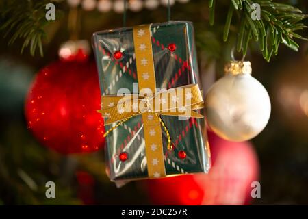 Geschmückter Weihnachtsbaum, echte Nordmann-Tanne vor verschwommenem Hintergrund. Makro-Fotografie zeigt verpackt handgemachte Geschenk. Stockfoto