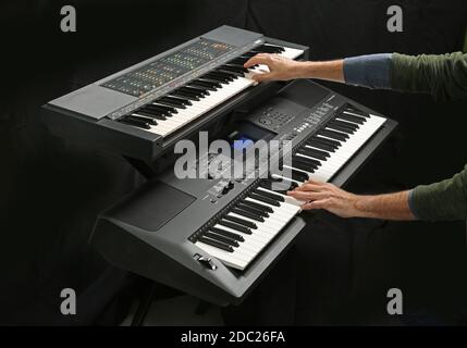 Studioaufnahme von zwei elektronischen Yamaha-Tastaturen, die gespielt werden; Modelle PSR 70 (oben) und EW400. Abgebildet auf einem klappbaren X-Frame-Ständer aus Metall. Stockfoto