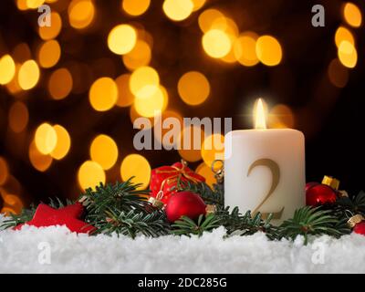 Kerze des zweiten Advents brennt, Tannenzweige und Weihnachtsbaumkugeln im Schnee Stockfoto