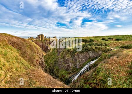 DUNNOTTAR CASTLE STONEHAVEN ABERDEENSHIRE SCHOTTLAND SONNENLICHT AUF DEN GEBÄUDEN UND KLIPPEN EIN GROSSER WASSERFALL IM VORDERGRUND Stockfoto