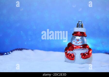 Schneemann mit rotem Schal im Schnee und blauem Himmel von hinten. Unscharfer Hintergrund. Frohe Weihnachtskarte. Neujahr Bokeh. Speicherplatz kopieren Stockfoto