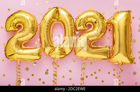 2021 Jahre goldene Luftballons auf Bändern mit Konfetti an rosa Wand. Frohes neues Jahr 2021 Eve Feier Stockfoto