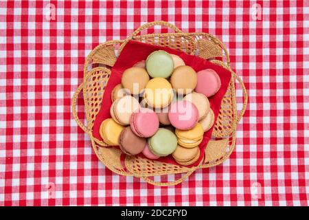 Gebäck, Desserts und Süßigkeiten. Draufsicht auf multicolord original französische Makronen-Kekse sind in einem Korb auf einer rot karierten Serviette angeordnet. Party, bi Stockfoto