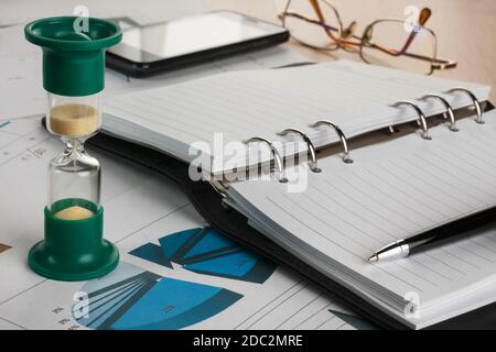 Sanduhr, Tagebuch, Stift, Gläser und Telefon, liegend auf einem Hintergrund von Diagrammen und Graphen Stockfoto