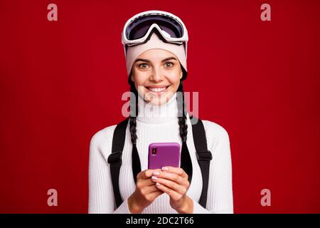 Foto von jungen schönen ziemlich lächelnd fröhliche Mädchen Skifahrer Surfen Im Telefon während der Winterferien isoliert auf rotem Hintergrund Stockfoto