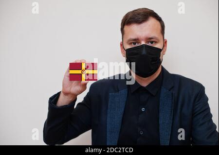 Mann tragen schwarz formell und schützen Gesichtsmaske, halten Northamptonshire Flagge Karte isoliert auf weißem Hintergrund. Vereinigtes Königreich Grafschaften von England coronavi Stockfoto