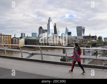 Eine Frau, die eine schützende Gesichtsmaske trägt, geht auf der Millennium Bridge mit der City of London im Hintergrund, während die zweite nationale Sperre sich in England ergreift. London, Vereinigtes Königreich November 2020. Stockfoto