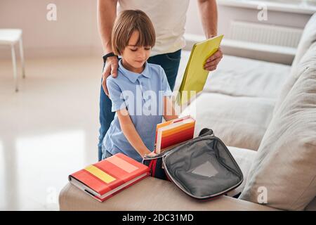 Fürsorglicher Vater hilft seinem kleinen Sohn, eine Schultasche zu packen Stockfoto