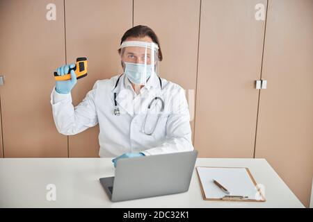 Professionelle Sanitäter mit einem Thermometer in der Hand posiert im Büro Stockfoto