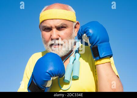 Ältere Mann Boxen - Nahaufnahme Porträt. Schöner älterer Mann, der Boxkick übt. Älterer Sportmann mit Boxhandschuhen. Lustiger bärtiger Mann steht Stockfoto