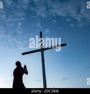 Mann, der unter dem Kreuz auf dem Gipfel des Berges betet Stockfoto