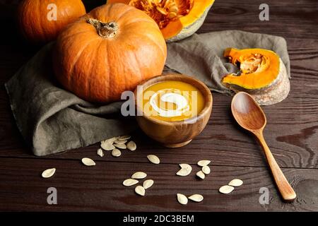 Kürbissuppe mit Sauerrahm auf rustikalem Holztisch. Herbst Kürbissuppe in Schüssel mit frischem Gemüse und Samen. Stockfoto