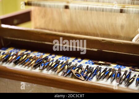 Eine Sammlung von Holz- blau und beige Webschützen auf der Vorderseite des traditionellen burmesischen Garn Motor. Flaches Tief, Seidenfäden im Hintergrund. Stockfoto