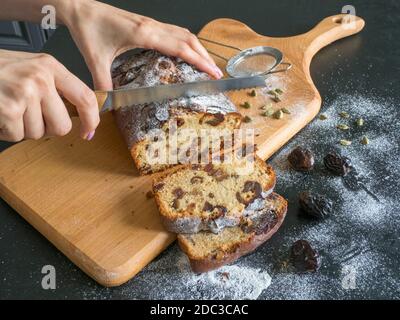 Das Schneiden der Stücke von Dattkuchen. Hausgemachte Datteln Brot mit Walnüssen auf einem schwarzen Tisch. Stockfoto