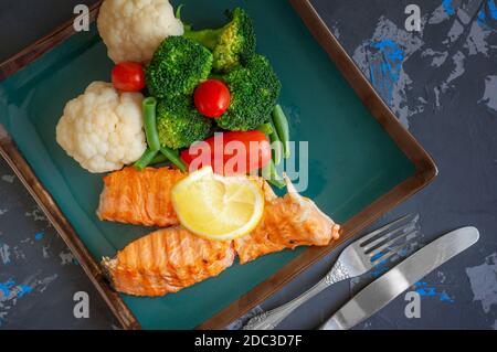 Diät Servieren von Lachs mit Zitrone, Brokkoli und Gemüse. Zwei Stücke gegrillter Lachs werden auf einem schönen Teller serviert. Stockfoto