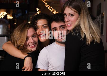 Drei lächelnde junge Frauen und ein ernsthafter junger Mann umarmten sich gegenseitig in einer Bar. Gruppe von Freunden. Stockfoto