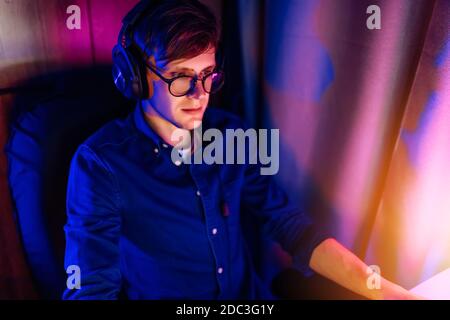 Ein glücklicher junger Gamer mit Brille und Headset spielt zu Hause Computerspiele. Technologie, Spiele, Unterhaltung Stockfoto