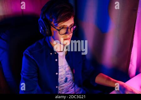 Ein glücklicher junger Gamer mit Brille und Headset spielt zu Hause Computerspiele. Technologie, Spiele, Unterhaltung Stockfoto