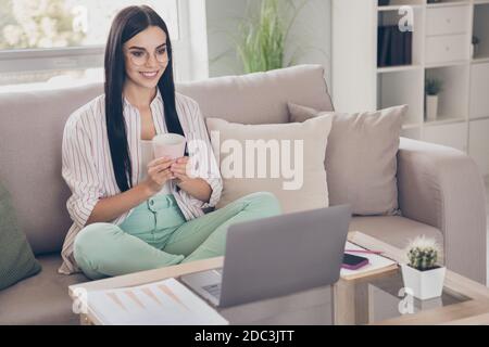 Porträtfoto von jungen Arbeiterinnen mit Laptop zu Hause Lächelnd halten Tasse mit warmen Getränk tragen Brille Lesen Stockfoto