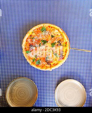 Runde Pizza mit rotem Fischkäse und Rucola auf einer karierten Tischdecke mit zwei Tellern. Draufsicht Stockfoto