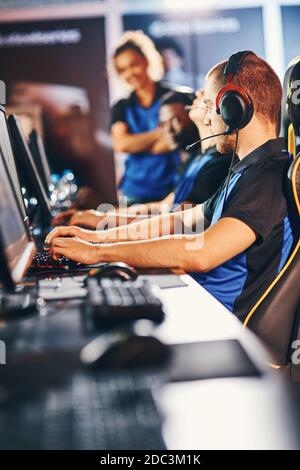 Online-Videospiele spielen. Professionelle Cybersport-Spieler, die Kopfhörer tragen, sitzen in einer Reihe, die am eSport-Turnier teilnehmen, konzentrieren sich auf einen kaukasischen Kerl Stockfoto