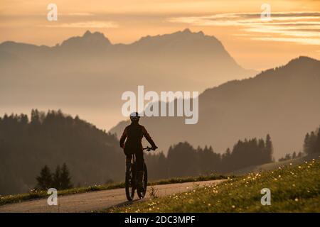Aktive Frau auf ihrem Elektro-Mountainbike bei Sonnenuntergang vor der atemberaubenden Silhouette des Saentis, Appenzell schweiz Stockfoto