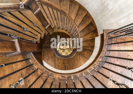 Eine Wendeltreppe mit Holztreppen / Handläufen und schmiedeeisernen Spindeln mit Fliesen am Boden. Stockfoto