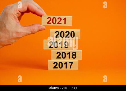 Männliche Hand, die einen Block mit der Nummer '2021' auf einen Turm mit den Nummern '2017, 2018, 2019, 2020' setzt. Schöner orangefarbener Hintergrund. Speicherplatz kopieren. Unternehmen Stockfoto