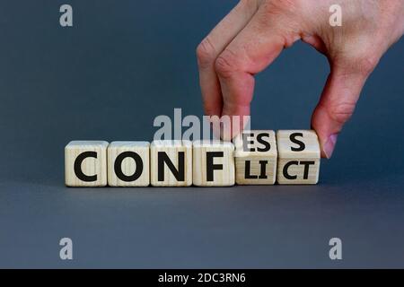 Hand dreht Würfel und ändert den Ausdruck 'Konflikt' in 'Geständnis' oder umgekehrt. Schöner grauer Hintergrund. Konzept. Speicherplatz kopieren. Stockfoto