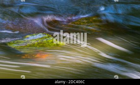 Natur Hintergrund der wilden Strom Detail fließt über moosigen Steinen. Abstrakte grüne oder blaue dynamische wellige Wasseroberfläche. Bewegungsunschärfe auf weißen Stromlinien. Stockfoto