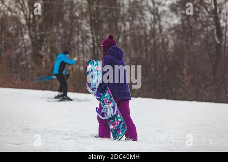 Frau, die mit Snowboard in lila Mantel bergauf geht Stockfoto