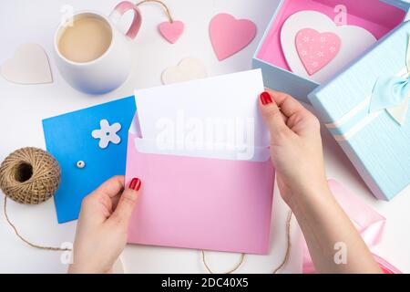 Hände einer Frau nehmen einen Brief aus einem rosa Umschlag auf einem romantischen Hintergrund. Stockfoto
