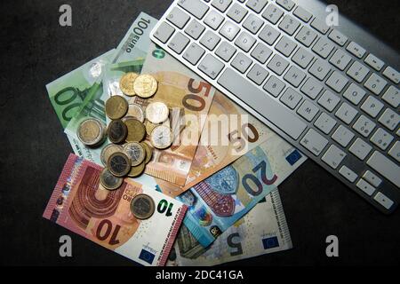 euro-Banknoten und -Münzen auf einer schwarzen Oberfläche mit dem Computertastatur Stockfoto