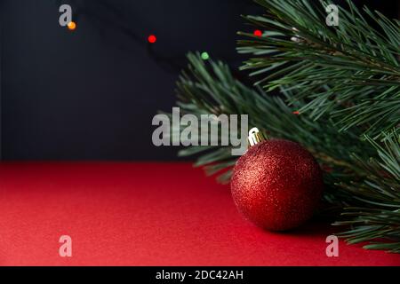 Grüne Kiefer Zweig und rot glänzenden Weihnachtskugel Nahaufnahme auf einem rot-schwarzen Hintergrund. Traditioneller Winterurlaub. Schönes Neujahr oder Weihnachten Backgro Stockfoto