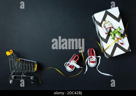 Shopping Trolley, rote Sneaker, Neujahrsgeschenk und goldenes Band auf schwarzem Hintergrund. Weihnachtseinkäufe, Verkauf, Rabatte. Schuhgeschäft. Vorlage für adv Stockfoto