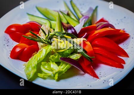 Frisches Gemüse für den Snack.Süße rote Paprika, Tomaten, grüne Gurken, Salat Salat serviert auf Weiße Keramikplatte im Café Stockfoto