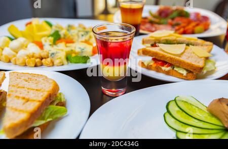 Snacks & Shots in der Bar.Tisch mit Snack-Essen und stark Alkoholische Getränke für Party. Mehrfarbiger mexikanischer Shot Drink, Club Sandwiches, frische Salate serviert Stockfoto