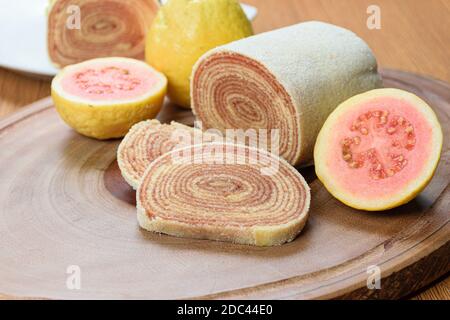 Scheiben von bolo de rolo (Brötchen Kuchen) neben guavas auf einem Holzbrett. Stockfoto