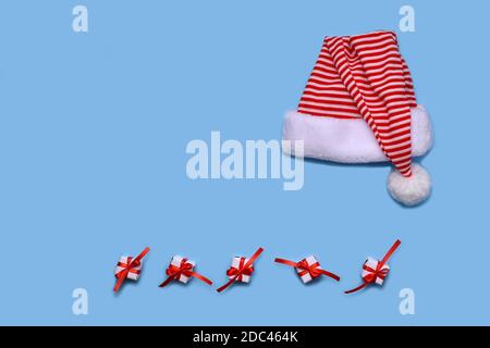 Der gestreifte Hut des Weihnachtsmannes, auf blauem Hintergrund angelegt. Unten sind weiß tapeziert Geschenke und bandagierte rote Band mit einer Schleife. Stockfoto