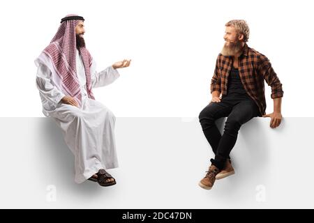 Arabischer Mann in einem Khobe und ein bärtiger Kerl Hipster Sitzt auf einer Tafel isoliert auf weißem Hintergrund sprechen Stockfoto