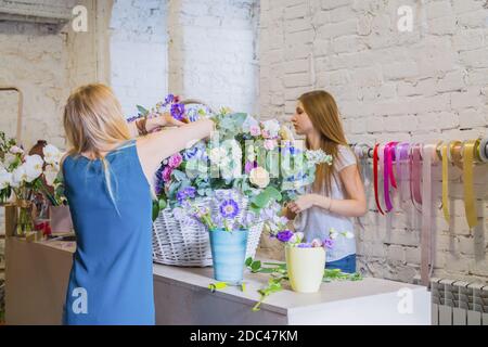 Zwei Damen Floristen machen großen Blumenkorb mit Blumen im hellen Raum Stockfoto