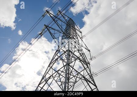 Low-Angle-Bild eines elektrischen Transmissionsgitterturms. Hochspannungsleitungen gegen den sommerlichen Himmel. Abstandshalter hängen vom Turm Stockfoto