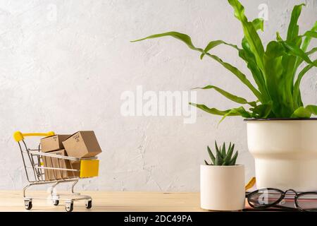 Spielzeug-Warenkorb mit Boxen auf dem Holztisch mit schönen Kakteen und Pflanzen im Design Betontöpfe. Graue Wände. Einkaufskonzept. Stockfoto