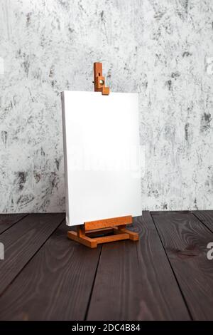 Weiße leere synthetische Leinwand auf Hilfsrahmen gestreckt und eine Staffelei auf einem braunen Holztisch stehen Stockfoto