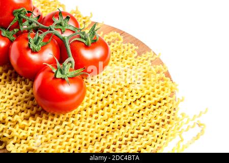 Haufenfusilli bucati lunghi italienische Pasta und frische rote reife Tomaten auf einem grünen Zweig, der auf Holzbrettbuche liegt. Isoliert auf weißem Hintergrund Stockfoto