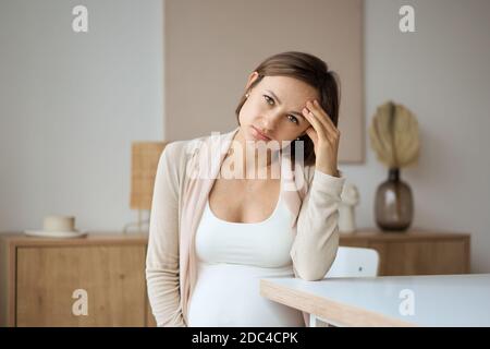 Schwangere Frau, die an Kopfschmerzen leidet, während sie am Tisch sitzt Stockfoto