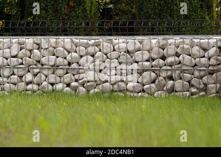 Beeindruckende Art und Weise der Einzäunung des Gartens, Metallkörbe mit weißen Kieselsteinen gefüllt. Stockfoto