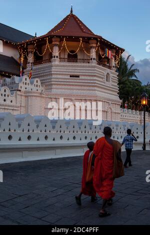 Buddhistische Mönche gehen am Tempel der Heiligen Zahnreliquie in Kandy in Sri Lanka in der Abenddämmerung vorbei. Stockfoto