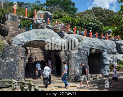 Eine Reihe buddhistischer Mönchsstatuen mit orangefarbenen Roben und Touristen gehen in Richtung des Goldenen Tempels in Dambulla in Zentral-Sri Lanka. Stockfoto